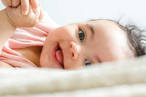 Little girl wearing a pink onesie smiling. Discover sustainable, affordable, gently-loved children's clothing bundles at Bundled, supporting parents and the environment with curated, high-quality options for newborns to toddlers at affordable and cheap price points.