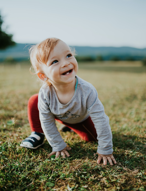 Boy wearing a grey shirt with red pants smiling while playing outside. Discover sustainable, affordable, gently-loved children's clothing bundles at Bundled, supporting parents and the environment with curated, high-quality options for newborns to toddlers at affordable and cheap price points.