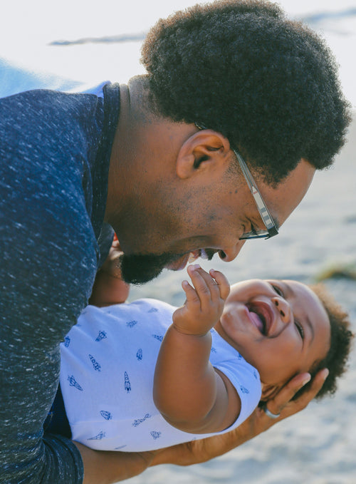 A dad and his son on the beach with a cute outfit on. Discover sustainable, affordable, gently-loved children's clothing bundles at Bundled, supporting parents and the environment with curated, high-quality options for newborns to toddlers at affordable and cheap price points.