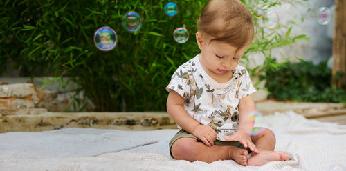 Little boy wearing a safari-styled outfit sitting playing with bubbles. Discover sustainable, affordable, gently-loved children's clothing bundles at Bundled, supporting parents and the environment with curated, high-quality options for newborns to toddlers at affordable and cheap price points.