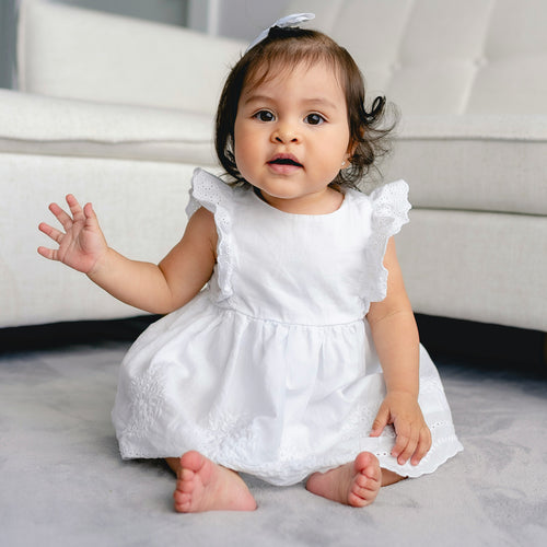 Little girl sitting wearing a white formal dress and waving. Discover sustainable, affordable, gently-loved children's clothing bundles at Bundled, supporting parents and the environment with curated, high-quality options for newborns to toddlers at affordable and cheap price points.