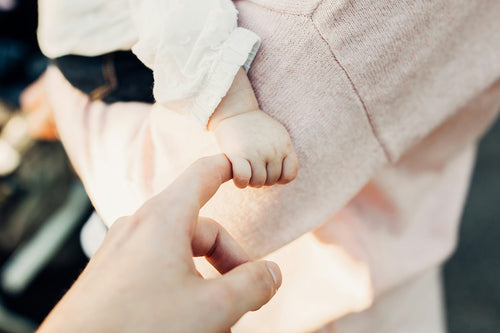 Cute picture of baby being held and holding onto a finger. Discover sustainable, affordable, gently-loved children's clothing bundles at Bundled, supporting parents and the environment with curated, high-quality options for newborns to toddlers at affordable and cheap price points.