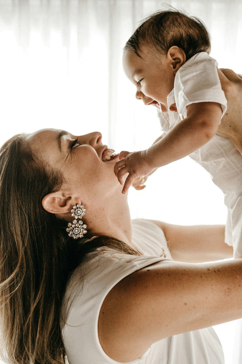 Mom holding her little newborn baby boy in the air and smiling at each other. Discover sustainable, affordable, gently-loved children's clothing bundles at Bundled, supporting parents and the environment with curated, high-quality options for newborns to toddlers at affordable and cheap price points.