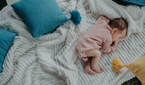 Newborn baby on a blanket with blue, white and yellow tones. Discover sustainable, affordable, gently-loved children's clothing bundles at Bundled, supporting parents and the environment with curated, high-quality options for newborns to toddlers at affordable and cheap price points.