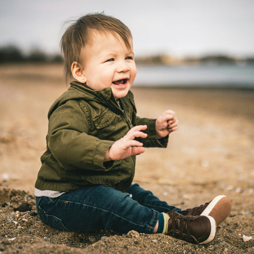 Toddler boy sitting on the ground wearing a jacket. Discover sustainable, affordable, gently-loved children's clothing bundles at Bundled, supporting parents and the environment with curated, high-quality options for newborns to toddlers at affordable and cheap price points.